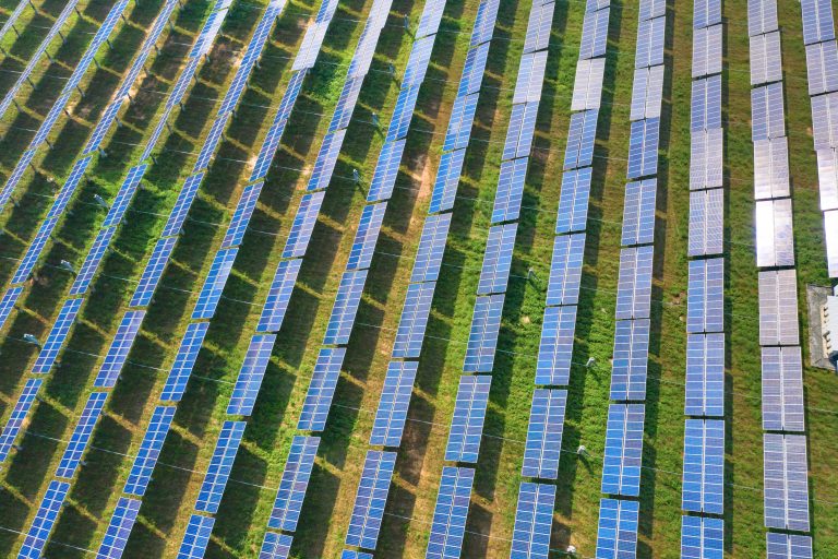 Aerial view of solar panels or solar cells on the roof in farm. Power plant with green field, renewable energy source in Thailand. Eco technology for electric power in industry.